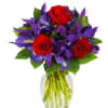 Bouquet of red roses and purple flowers in a clear glass vase