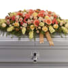 Large floral spray on a silver casket with peach and yellow blooms