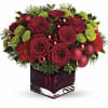 Red roses and green pom flowers in a red glass vase with ornaments