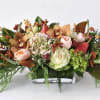 Low rectangular centerpiece with peach roses, orchids, hydrangea, berries, and evergreen accents in a glass vase