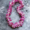 Purple and white orchid flower lei arranged in an oval on a gray stone surface