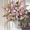 Tall arrangement of pink roses, carnations, and white flowers in a white urn on a pedestal