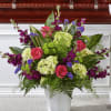 Tall arrangement of pink roses, green hydrangeas and purple flowers in a white container