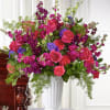 Tall pink and purple rose and carnation arrangement with trailing greenery in a white urn