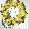 Large yellow and white floral wreath with ivy displayed on a metal easel stand