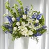 Tall white and blue arrangement with lilies, roses, delphinium and Bells of Ireland in a white pedestal vase.