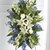 Tall standing spray of white lilies, roses, and blue flowers on a metal easel