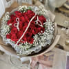 Hand-tied bouquet of red roses and white filler flowers wrapped in paper with draped pearl strands.