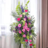 Tall standing spray with pink roses, purple flowers, and green accents on an easel.