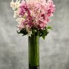 Tall cylinder vase of pink and white orchids with looped green foliage and stones at the base