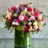 Large arrangement of pink roses, peonies, orchids, and green hydrangeas in a clear glass cylinder vase
