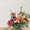 Pink lilies and roses in a glass vase with purple filler flowers