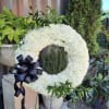 White floral wreath with a black ribbon bow on a stand