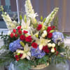 Large floral arrangement with red roses, white lilies, and blue hydrangeas in a basket