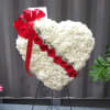 Standing heart-shaped white carnation wreath with diagonal red roses and a red ribbon bow on an easel