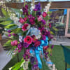 Tall floral standing spray with purple, pink, and blue flowers and a blue ribbon