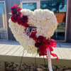 Heart-shaped white floral tribute with red flowers and ribbon