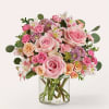 Pink roses and mixed blooms arranged in a clear glass vase