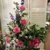 Tall bouquet of pink roses, purple flowers, and white blooms with a pink ribbon