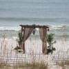 Beach wedding arch with draped curtains and chairs on the sand