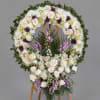 Large floral funeral wreath on a wooden easel with white, cream, purple, and green flowers.