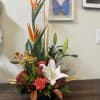 Tropical floral arrangement with white lilies and orange bird-of-paradise in a black container