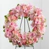 Pink floral wreath on a black stand with lilies, roses, and carnations