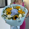 Bouquet of sunflowers, blue hydrangea, and white roses wrapped in pale blue paper