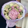 Bouquet of pink hydrangea, cream roses, and small white daisies wrapped in lavender paper