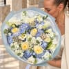 Woman holding a bouquet of blue and white flowers with pale yellow roses