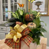 Fall plant arrangement in a white pot with plaid ribbon, pumpkins, and butterflies