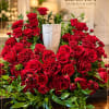 Large red rose arrangement in a white vase with trailing greenery