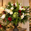 Holiday floral arrangement with white lilies, red roses, and evergreen in a dark urn