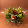 Orange and red floral arrangement in a low bowl with grasses