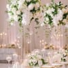 Tall white wedding centerpieces with orchids and roses on gold stands above a candlelit reception table
