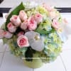 Pink roses and white orchids arranged with pale hydrangeas in a round vase