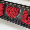 Red roses arranged in a black box with gold heart and letter outlines