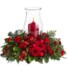 Red roses and carnations around a lit candle in a glass hurricane vase