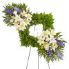 Heart-shaped floral wreath with white lilies and blue flowers on a stand