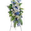 Tall standing floral spray with white lilies, white roses, and blue flowers