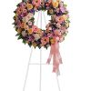 Pink and peach floral wreath on a white stand with a ribbon bow