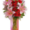 Pink lilies and red roses in a tall glass vase with a pink ribbon