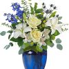 White roses and lilies in a blue glass vase with blue flowers