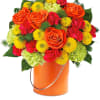 Mixed bouquet of orange roses, yellow mums, and pink carnations in an orange bucket