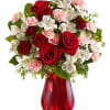 Red roses, white lilies, and pink carnations in a red glass vase
