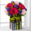 Bouquet of pink gerbera daisies, purple flowers, and pale pink roses in a decorative gift bag