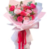 Bouquet of pink and blush roses wrapped in pale paper with a red ribbon