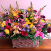 Large mixed basket arrangement with pink lilies, yellow roses, sunflowers, asters, and red carnations.