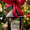 Decorative lantern with a red bow and Christmas message in front of a lit tree