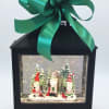 Black lantern with a large green bow and a Christmas gnome scene inside